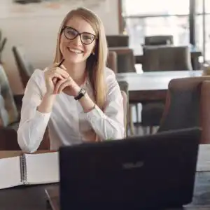 Segretaria Executive sorridente e sicura di sé, vestita da manager, alla scrivania mentre comunica con il CEO in un ufficio moderno.