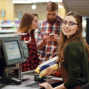 Cassiera sorridente mentre utilizza il registratore di cassa in un negozio, assistendo un cliente