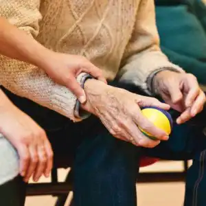 Assistente familiare che stringe la mano a un anziano durante un’attività riabilitativa con pallina antistress