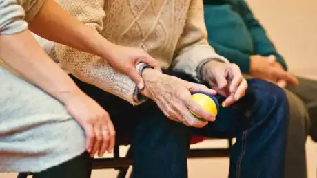 Assistente familiare che stringe la mano a un anziano durante un’attività riabilitativa con pallina antistress
