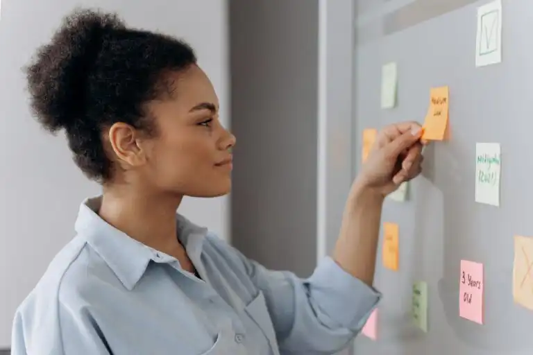 Giovane donna osserva post-it su una lavagna durante la pianificazione di un’attività professionale