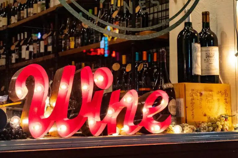 Insegna luminosa “Wine” in vetrina con bottiglie di vino e decorazioni