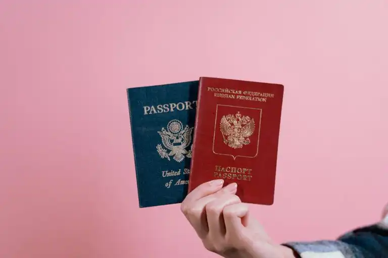 Due passaporti internazionali tenuti in mano su sfondo rosa, simbolo di viaggio e lavoro all’estero.